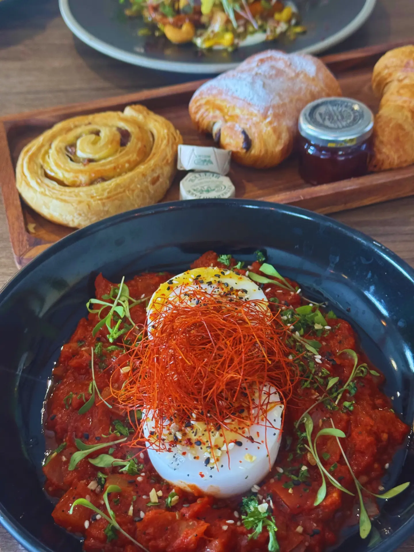 Shakshuka, baked egg in spiced tomato sauce topped with chilli threads and micro herbs, served with the Bakery Board