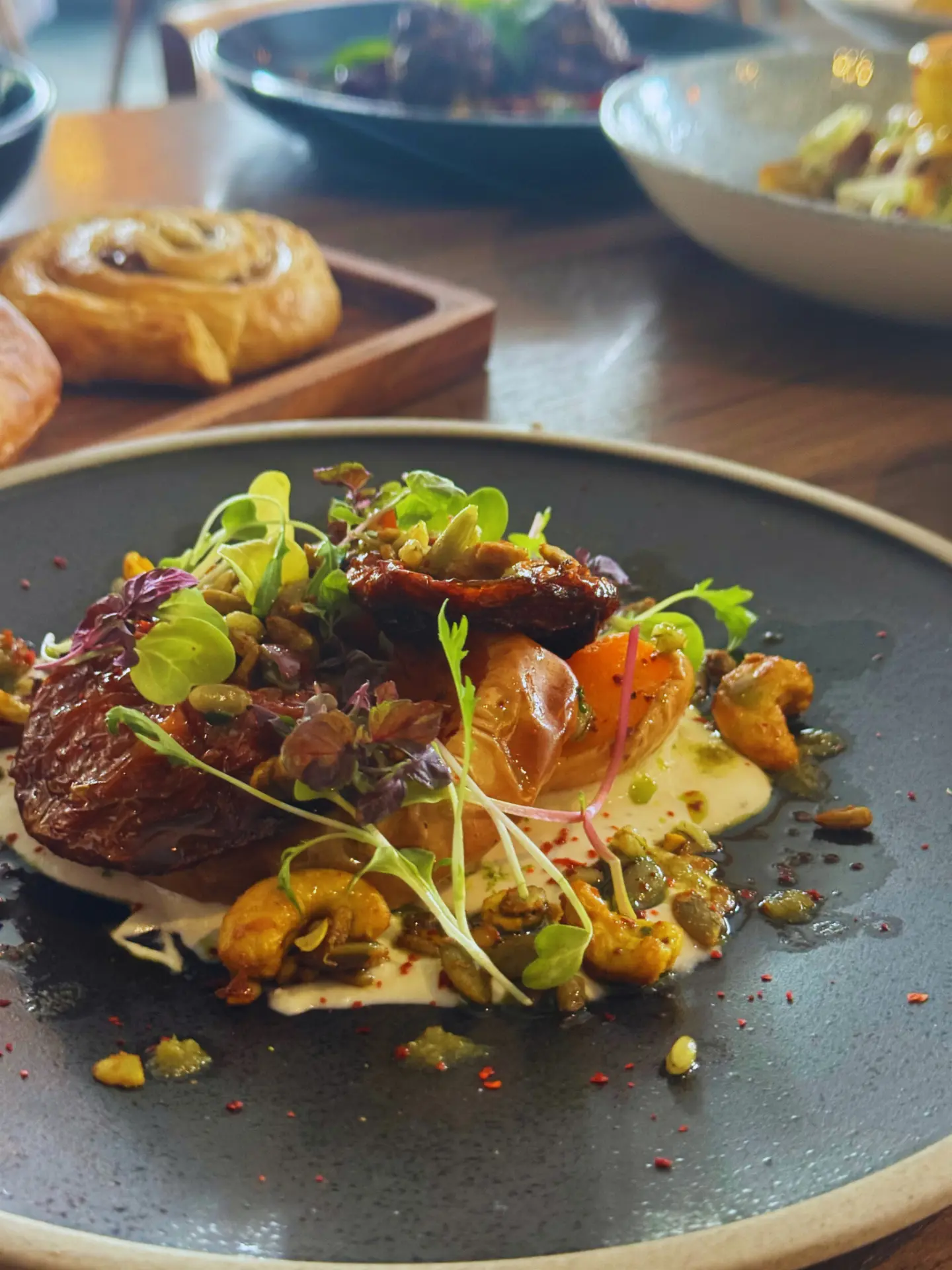 Roast butternut squash with spiced cashews, pumpkin seeds, micro herbs and whipped feta on a dark ceramic plate